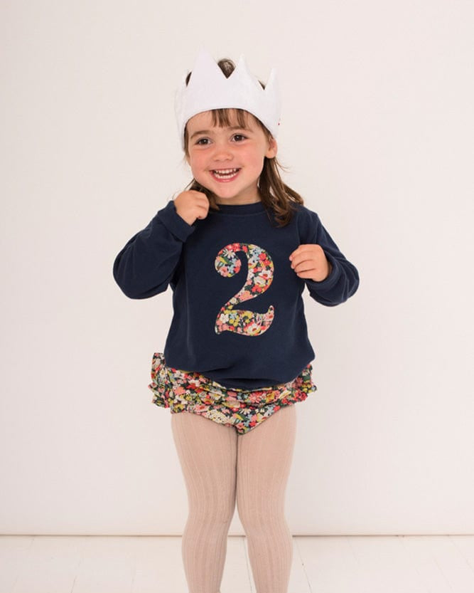 a 2 year old girl wearing a navy birthday t-shirt with a number 2 cut from thorpe floral liberty print on the front