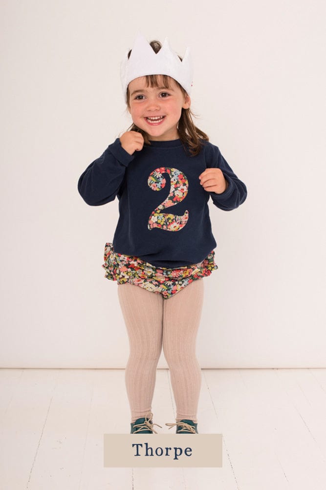 a 2 year old girl wearing a navy birthday t-shirt with a number 2 cut from thorpe floral liberty print on the front