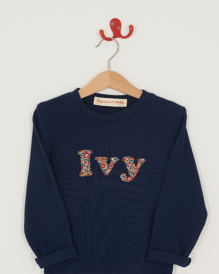 A personalised navy cotton t-shirt with the name Ivy on the front. The name is appliquéd in lowercase letters in Liberty floral fabric.