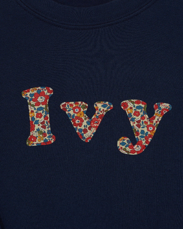 A personalised navy cotton t-shirt with the name Ivy on the front. The name is appliquéd in lowercase letters in Liberty floral fabric.