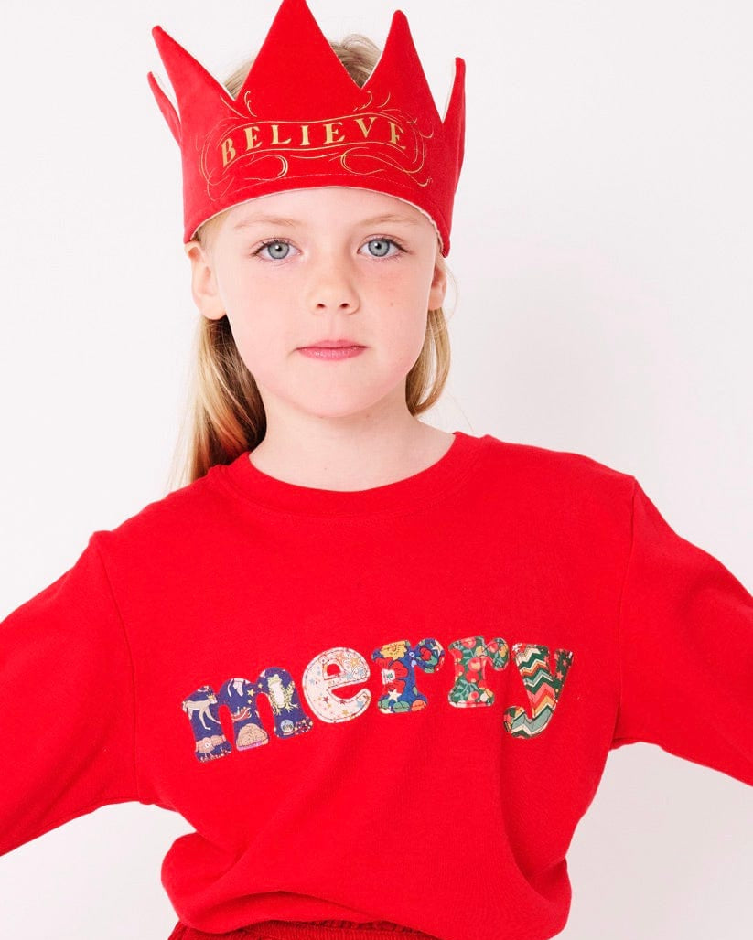 A smiling 5 year old girl wearing a red Christmas t-shirt that says Merry on the front, made from mixed liberty print fabrics.