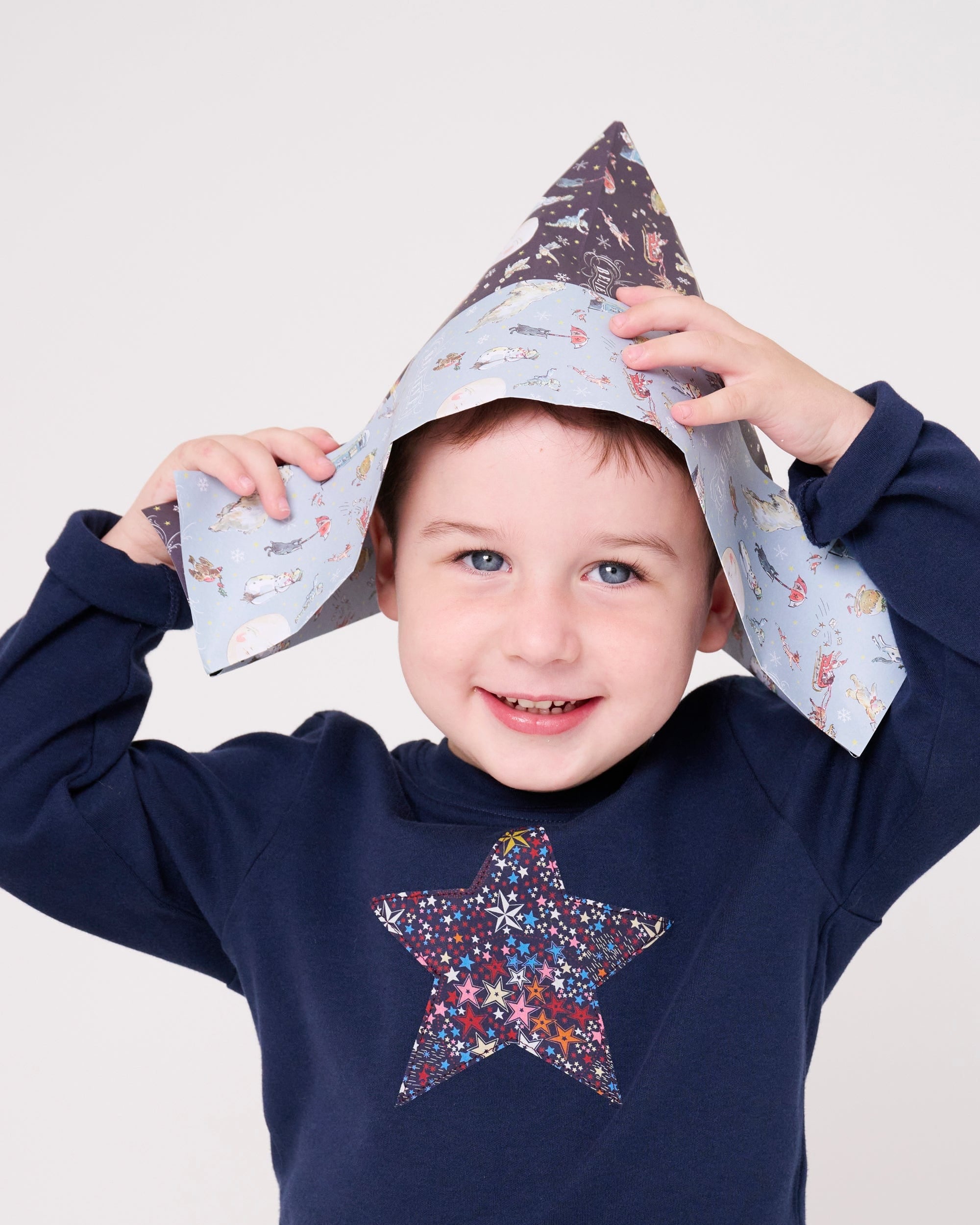 a 5 year old boy wearing a navy long sleeve christmas t-shirt with a festive star on the front made from Liberty Adelajda's Wish star print on the front.