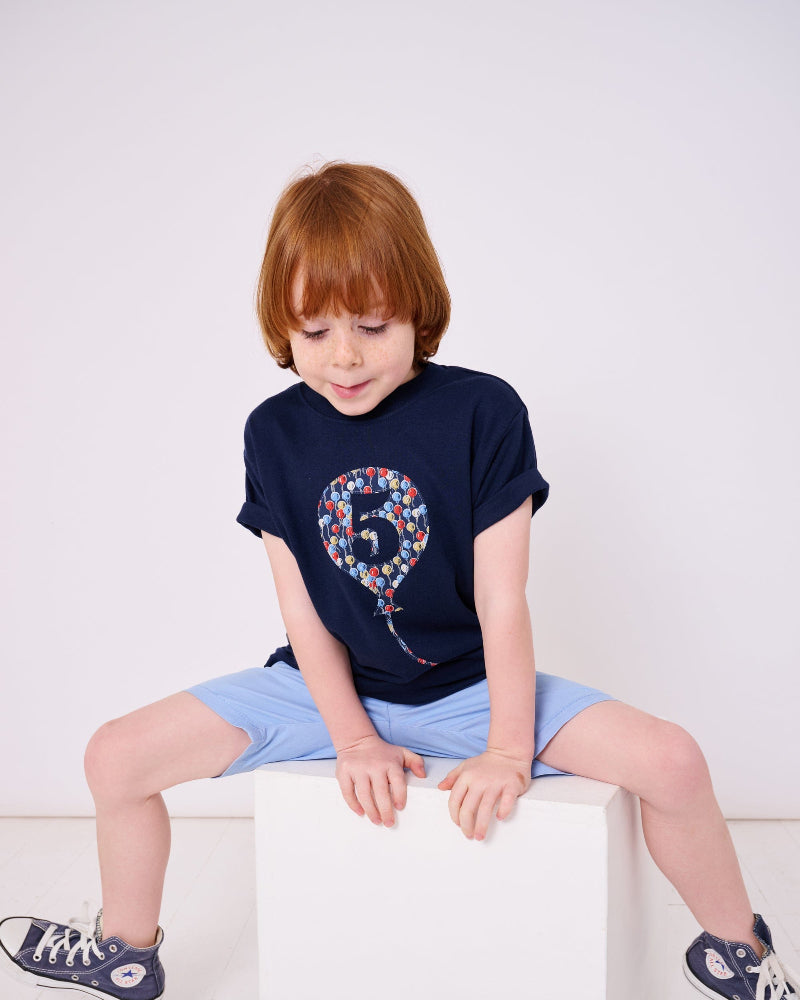 A 5 year old birthday boy wearing a navy t-shirt with a number 5 in a balloon on the front. The balloon is cut from Ethan's Party balloon Liberty print.