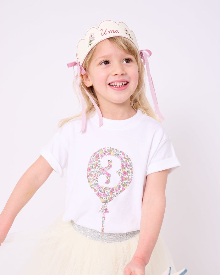A 3 year old girl wearing a 3rd birthday white t-shirt with a balloon and number 3 on it made from Liberty Floral print fabric.