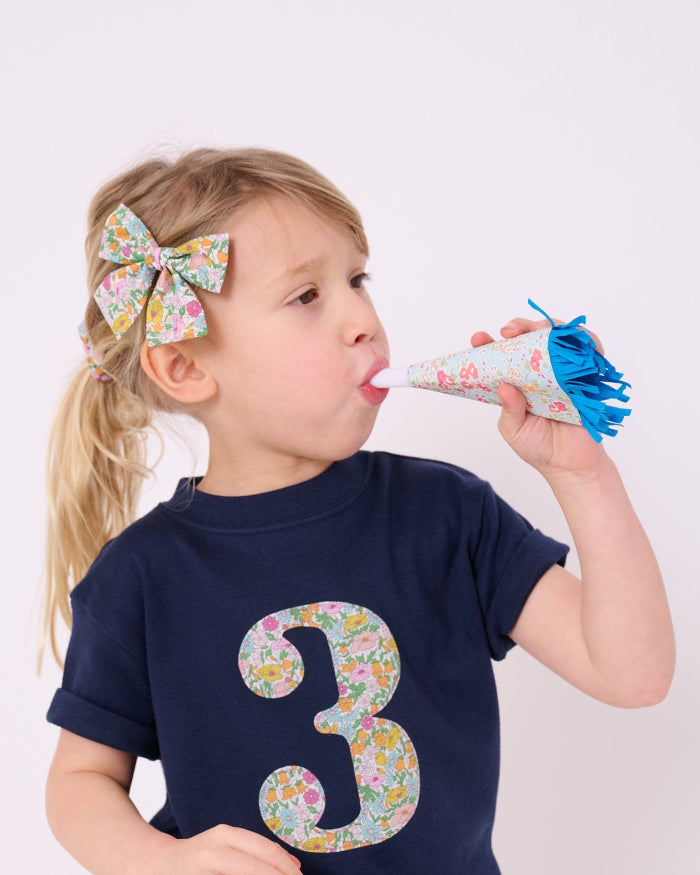 A 3 year old birthday girl wearing a Magnificent Stanley kids Number Navy T-Shirt in Poppy Forest Liberty Print.