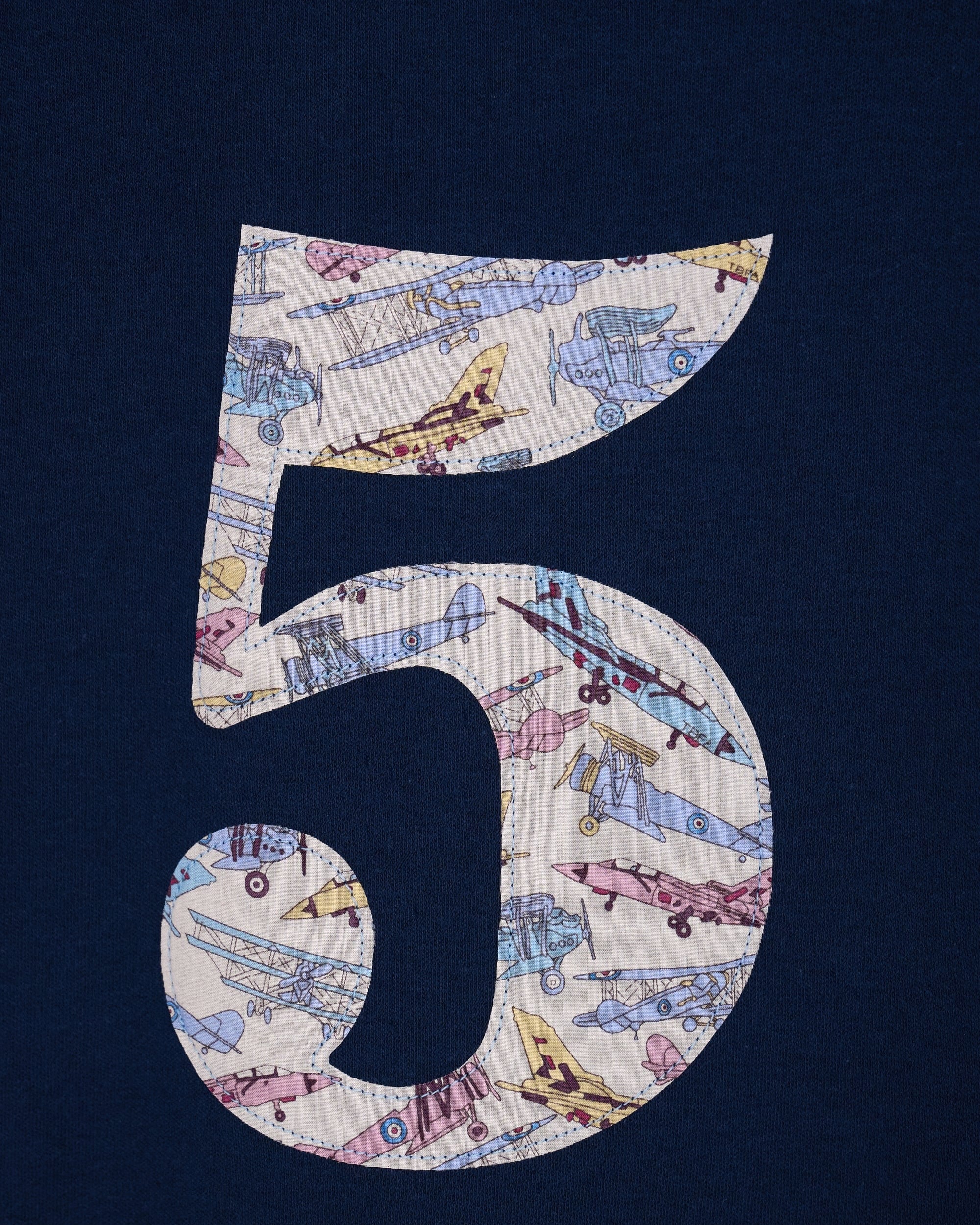 A close up of a navy cotton t-shirt with a number 5 sewn on the front made from Tom's Jet plane Liberty fabric.