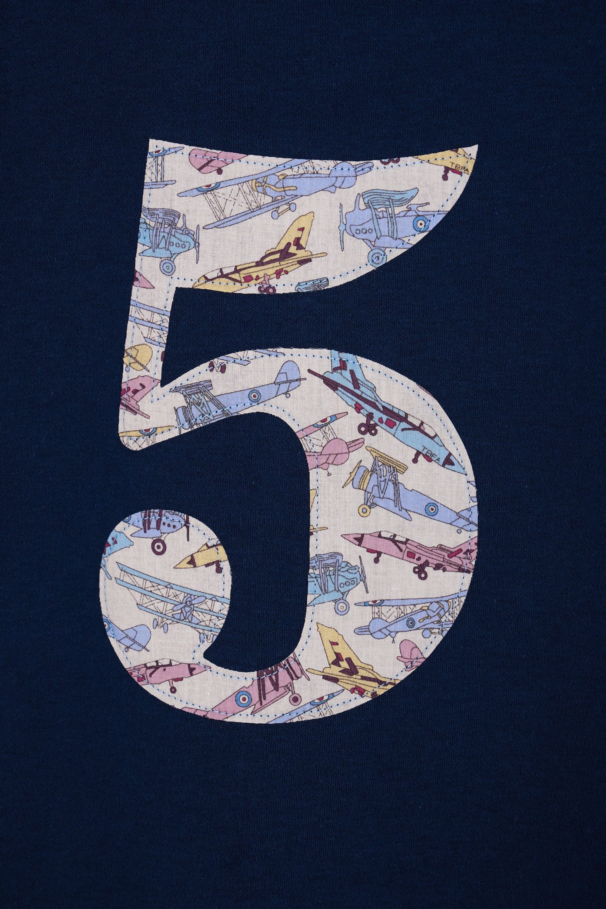 A close up of a navy cotton t-shirt with a number 5 sewn on the front made from Tom's Jet plane Liberty fabric.