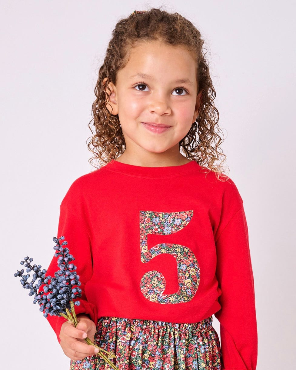 A 5 year old girl wearing a Magnificent Stanley long sleeve Red birthday T-Shirt with the number 5 on the front in Emma Louise floral Liberty Print
