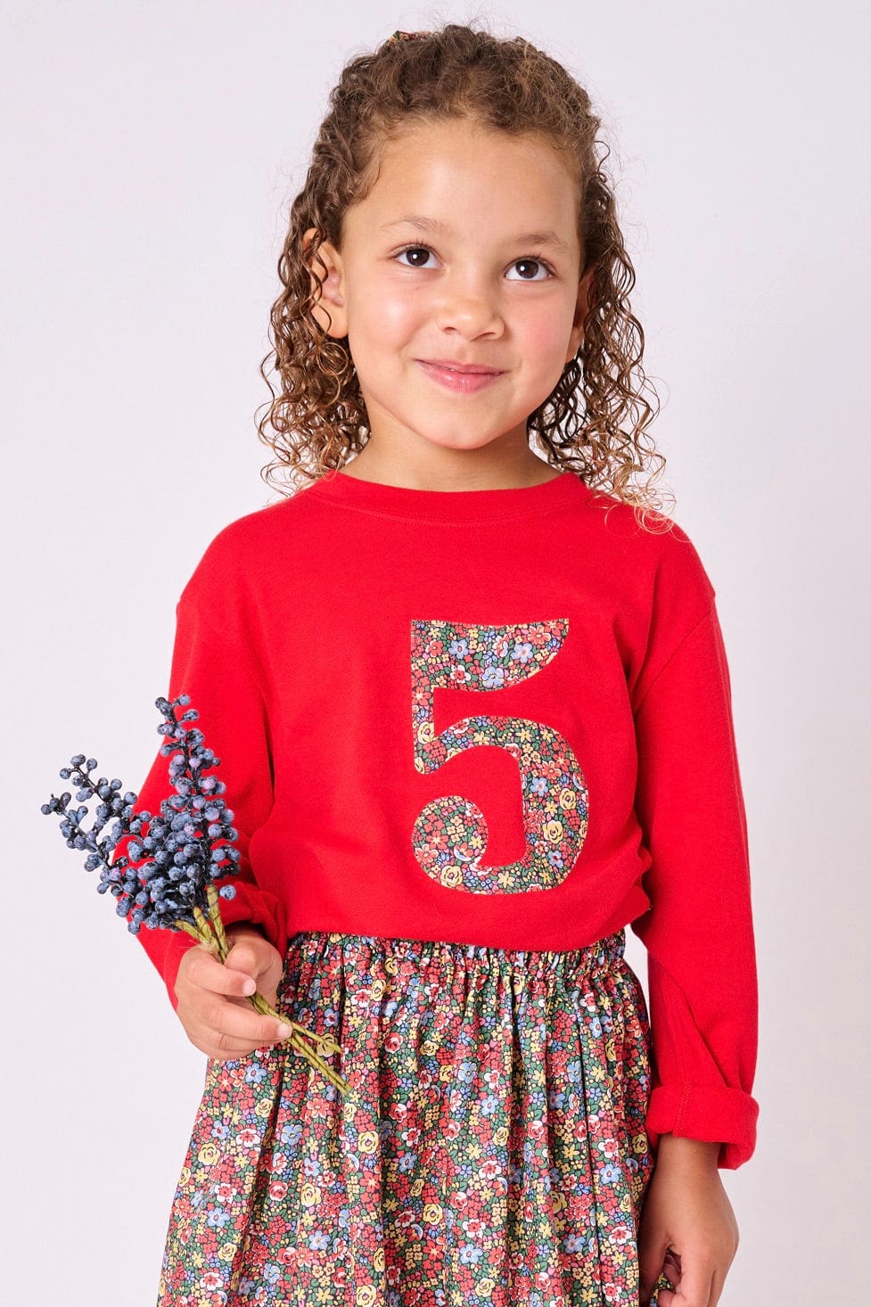 A 5 year old girl wearing a Magnificent Stanley long sleeve Red birthday T-Shirt with the number 5 on the front in Emma Louise floral Liberty Print