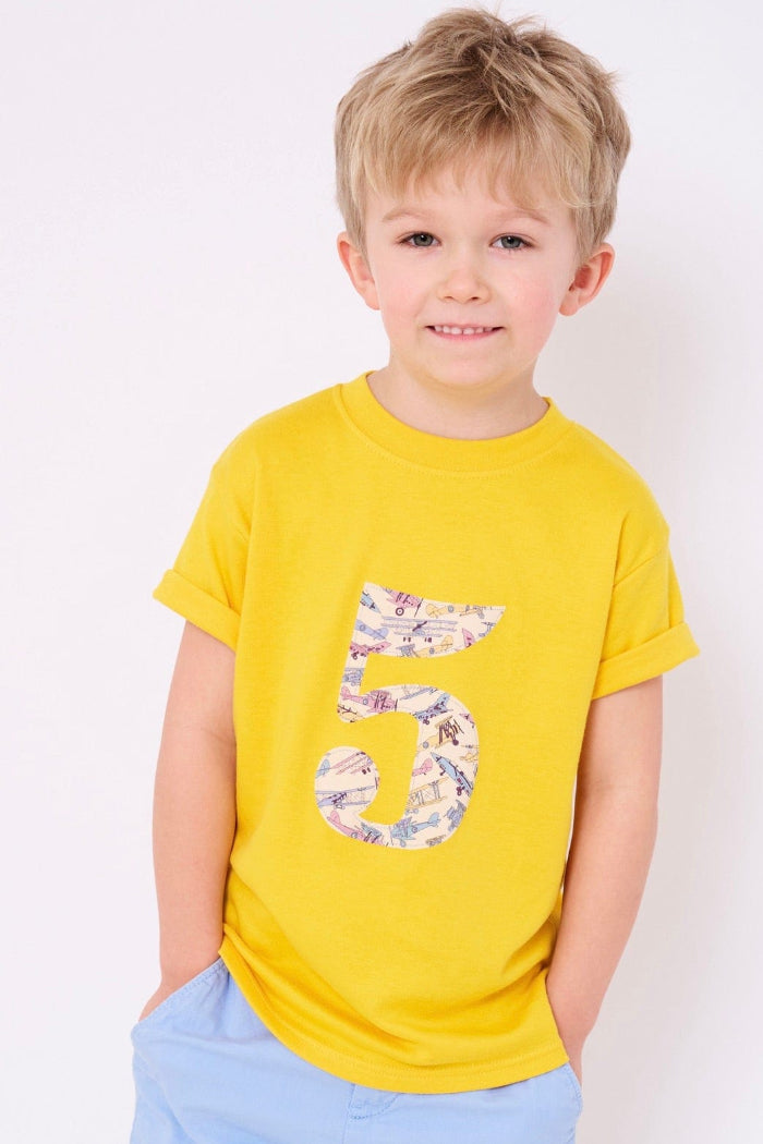 a 5 year old boy wearing a yellow cotton t-shirt with a number 5 sewn on the front made from Tom's Jet plane Liberty fabric.