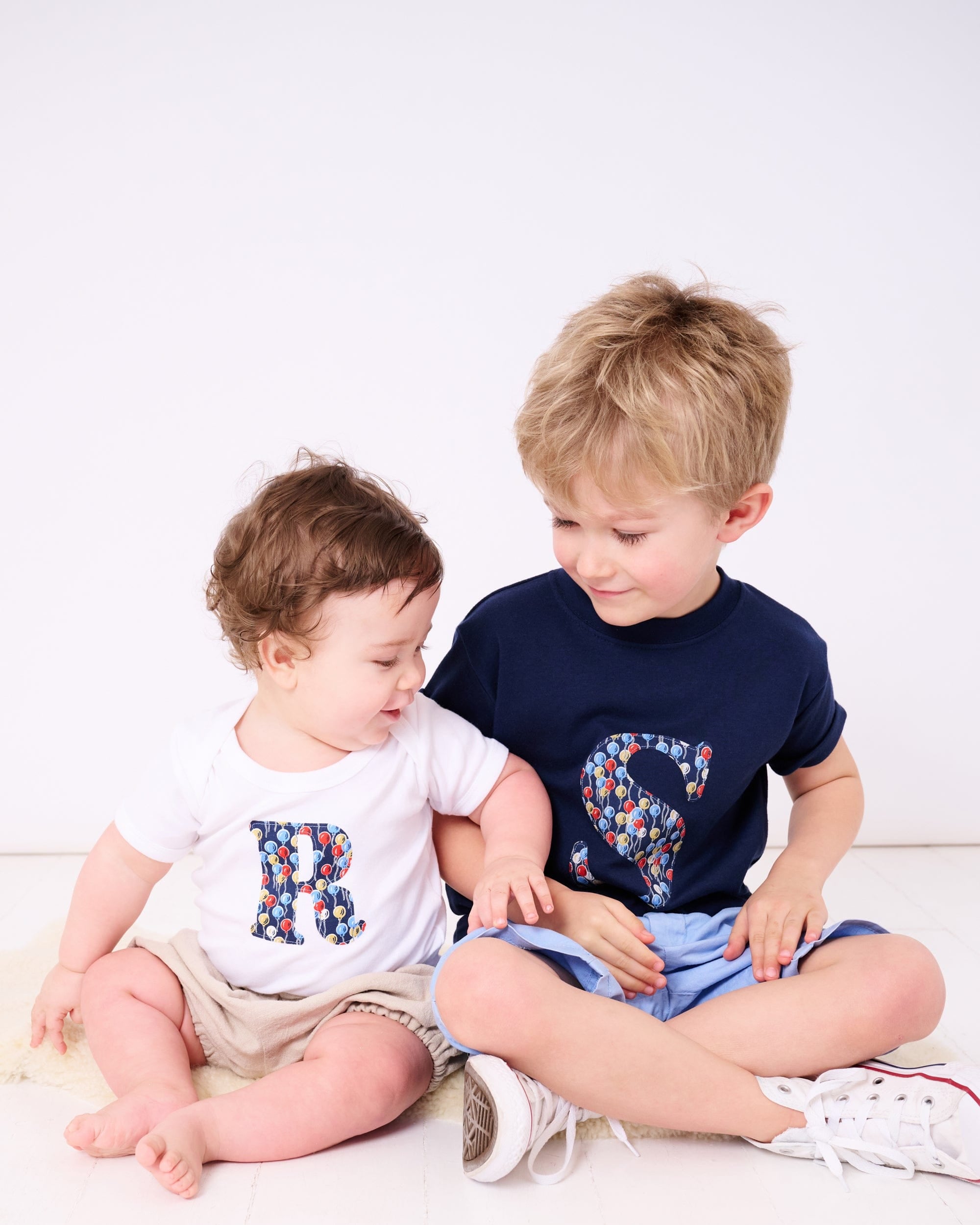 Siblings in matching personalised t-shirts with their initials in Liberty balloon print.