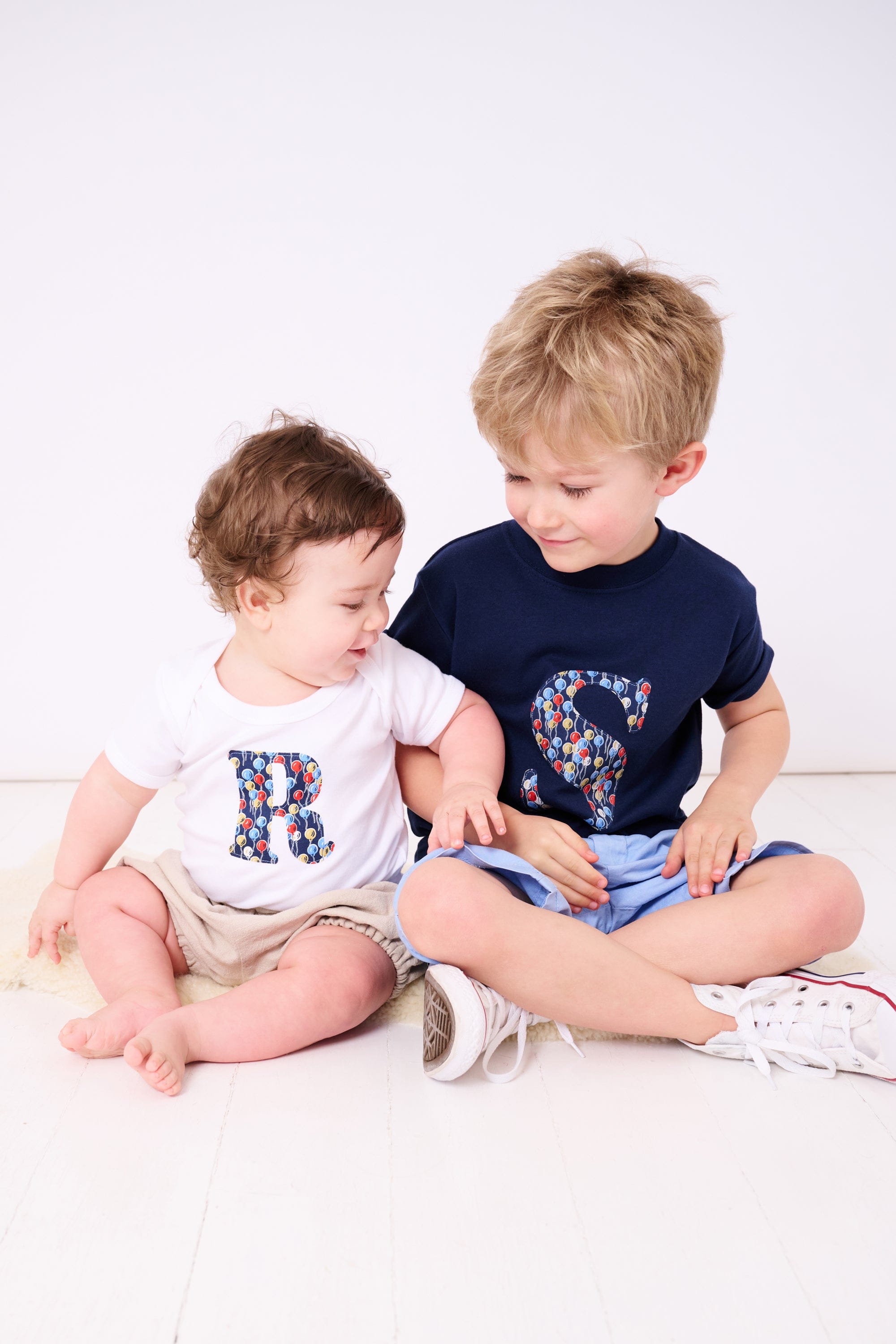 Siblings in matching personalised t-shirts with their initials in Liberty balloon print.