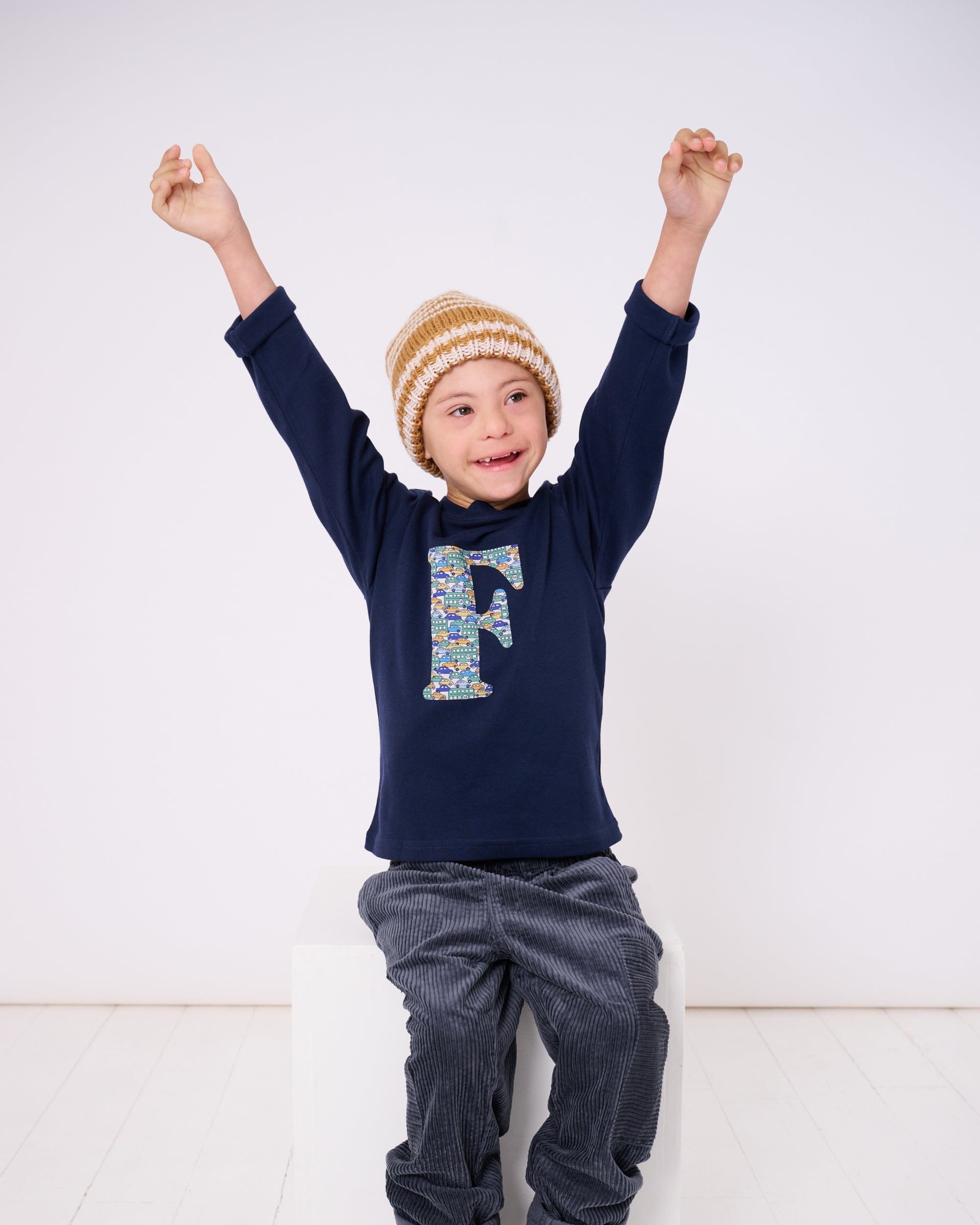 A happy 5 year old child wearing a personalised cotton long sleeve navy t-shirt with his initial on the front made from Liberty cars print.