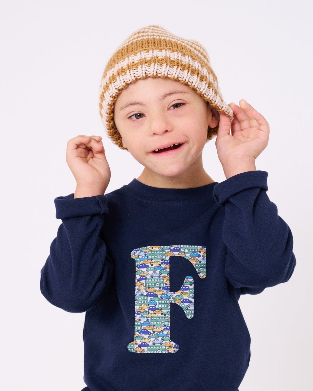 A happy 5 year old child wearing a personalised cotton long sleeve navy t-shirt with his initial on the front made from Liberty cars print.