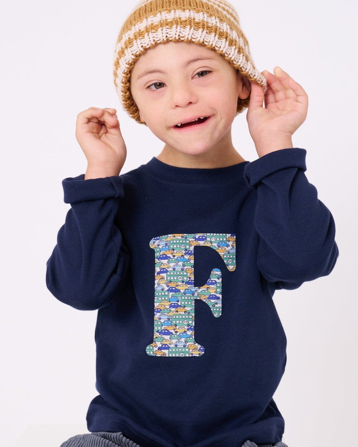 A happy 5 year old child wearing a personalised cotton long sleeve navy t-shirt with his initial on the front made from Liberty cars print.