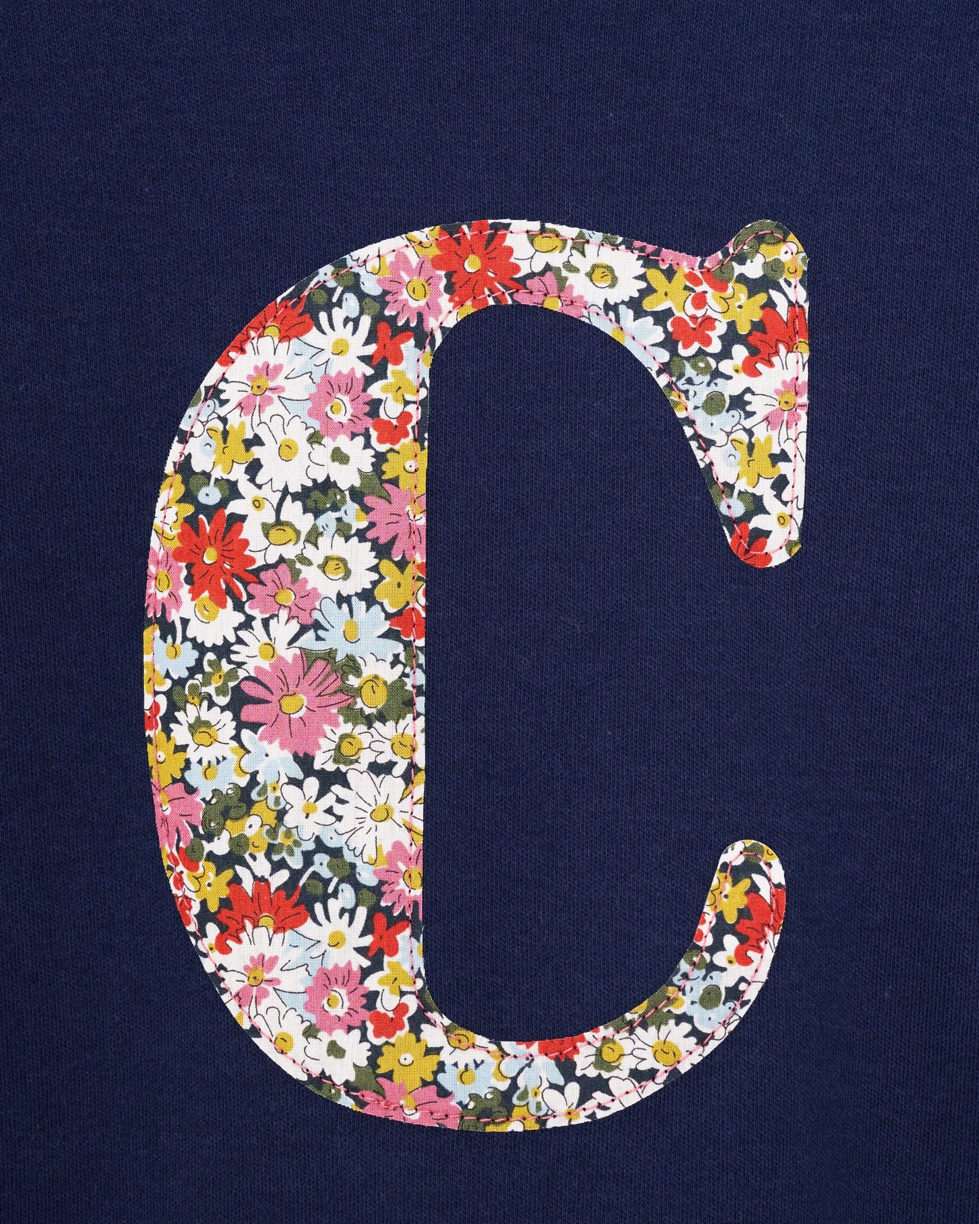A close up of a personalised cotton navy long sleeve t-shirt with her initial on the front made from Libby a floral Liberty print.