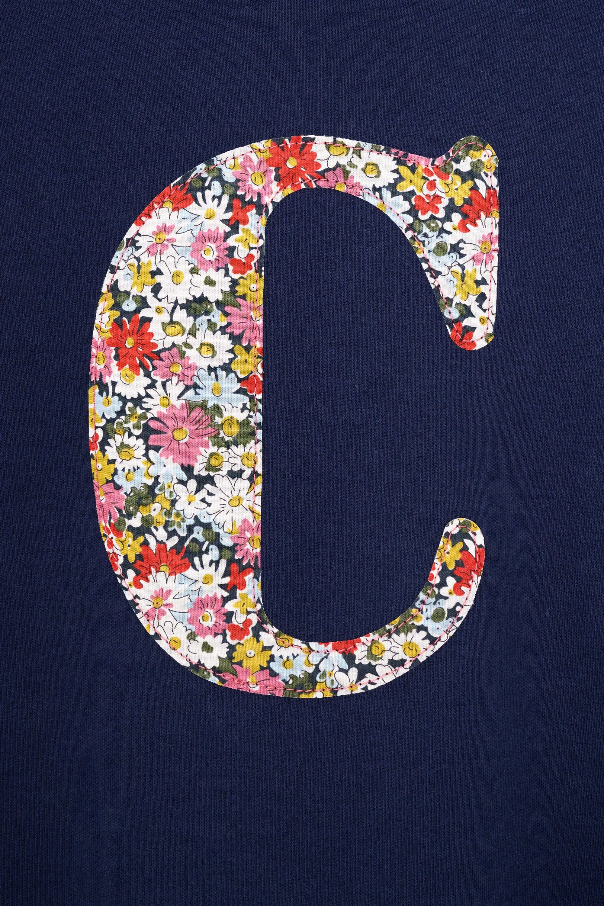A close up of a personalised cotton navy long sleeve t-shirt with her initial on the front made from Libby a floral Liberty print.