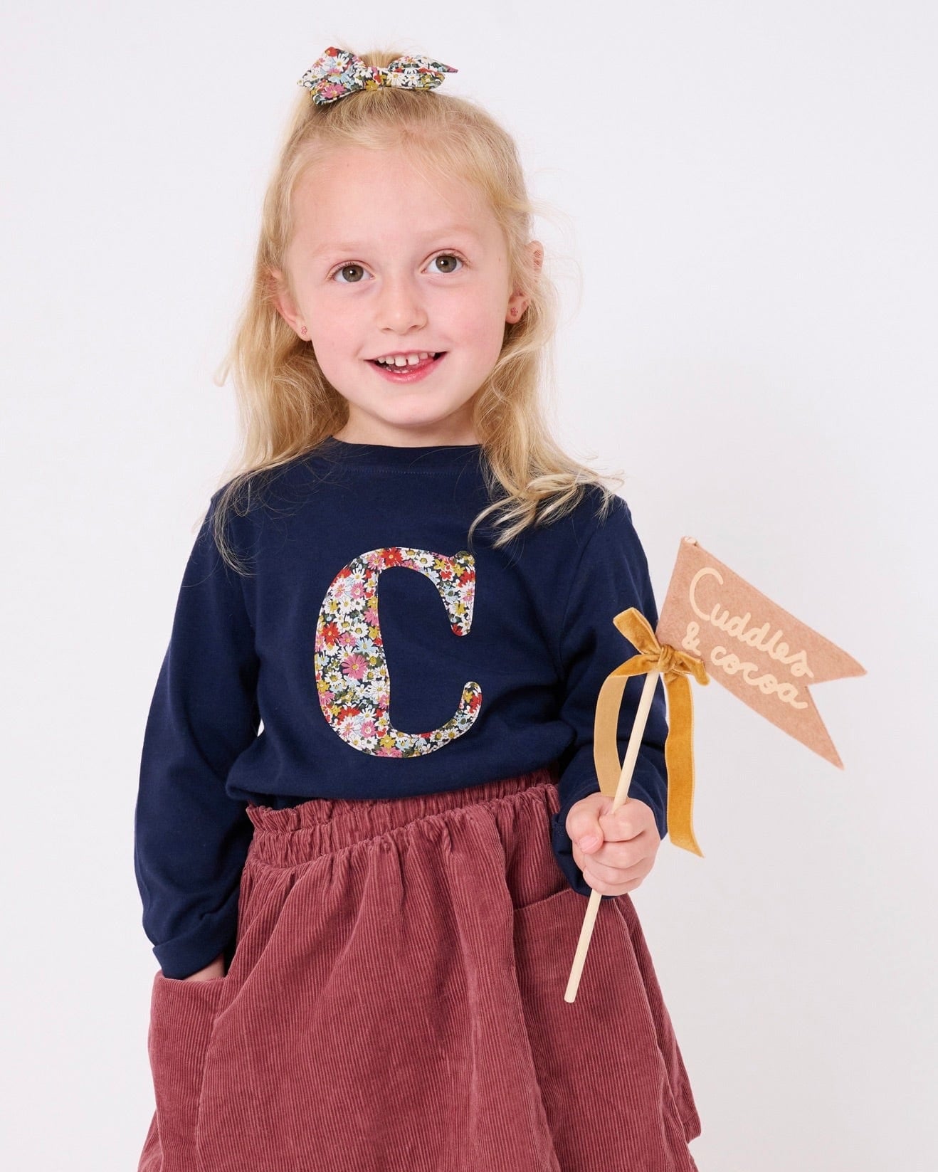 A 3 year old girl wearing a personalised cotton navy long sleeve t-shirt with her initial on the front made from Libby a floral Liberty print.