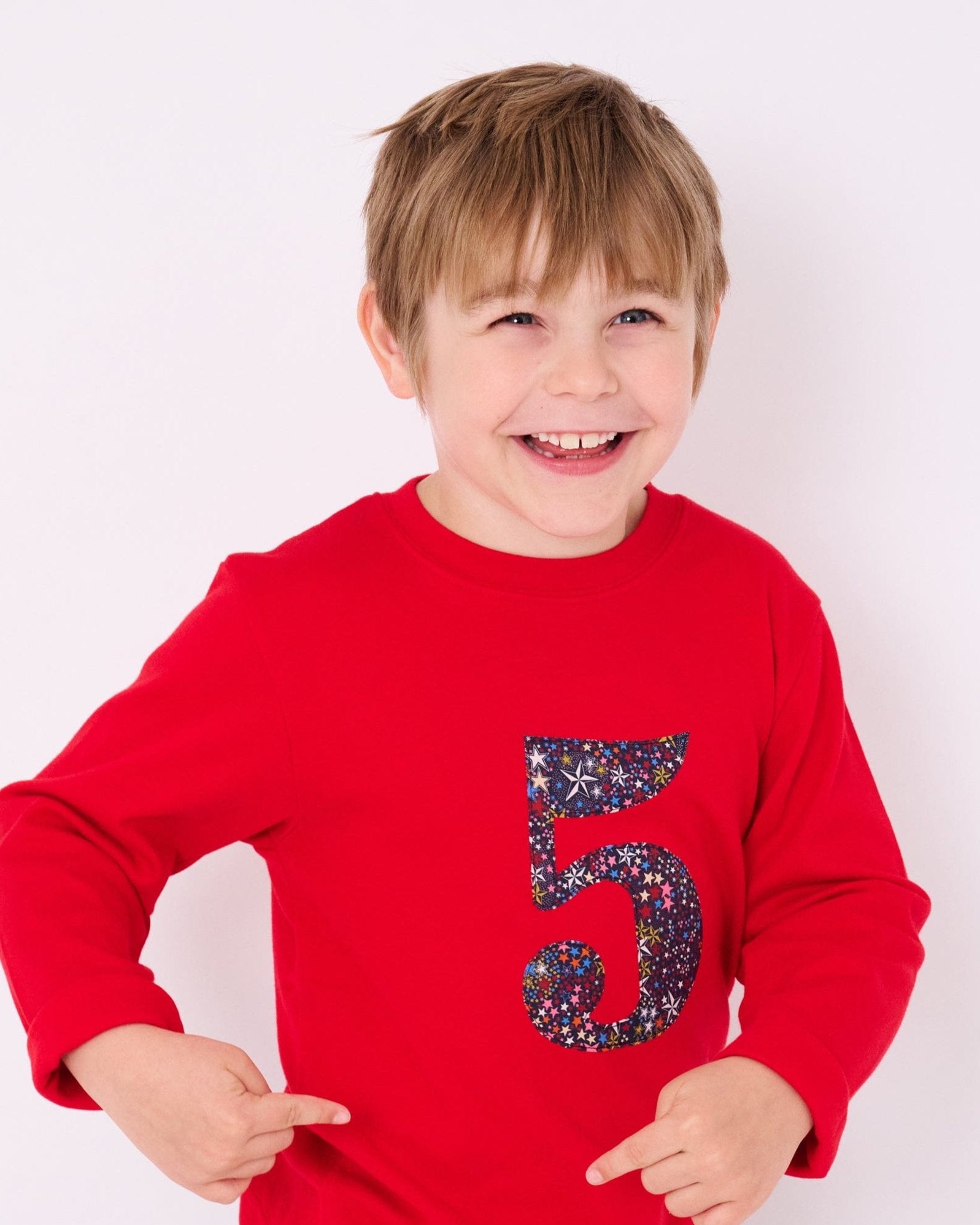 A smiling 5 year old boy wearing a red birthday t-shirt with the number 5 sewn onto it in Liberty Adelajda star print fabric.