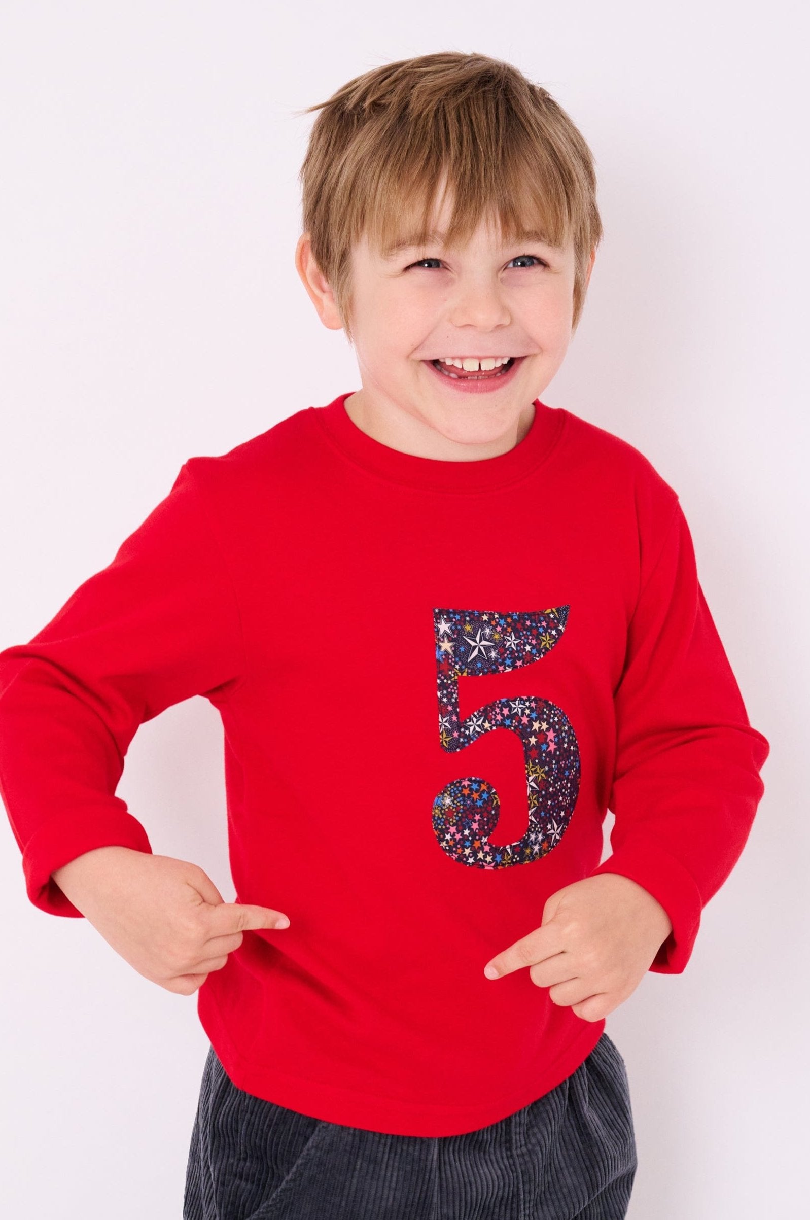 A smiling 5 year old boy wearing a red birthday t-shirt with the number 5 sewn onto it in Liberty Adelajda star print fabric.