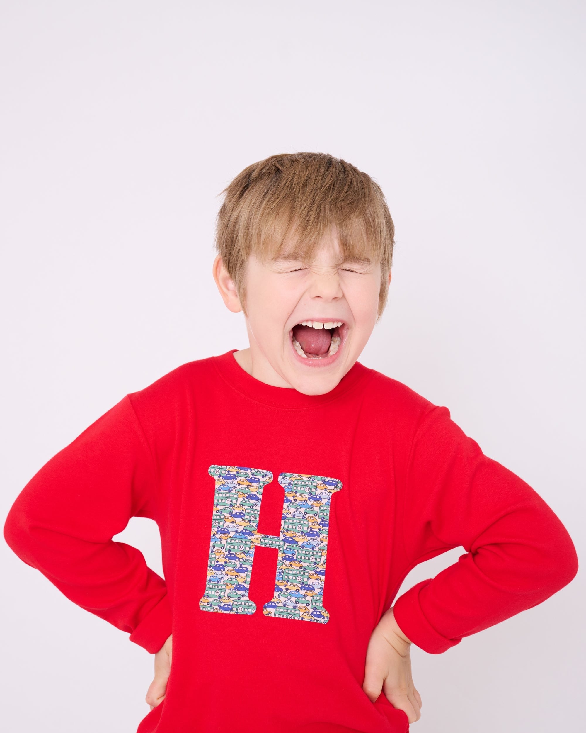 A 5 year old boy wearing a personalised red t-shirt with an initial made from a liberty vintage cars print on the front.