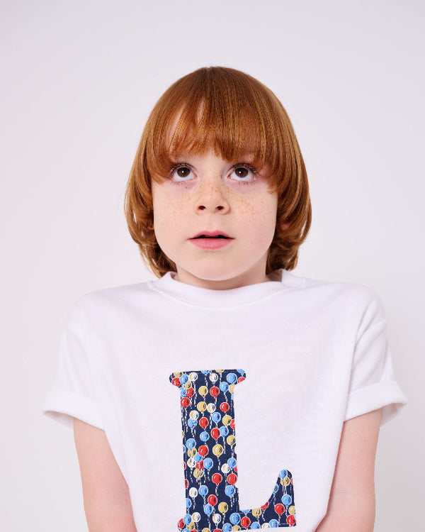 A 5 year old boy wearing a personalised white cotton T-Shirt in Ethan's Party balloon Liberty Print.