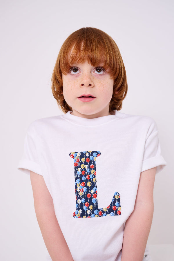 A 5 year old boy wearing a personalised white cotton T-Shirt in Ethan's Party balloon Liberty Print.