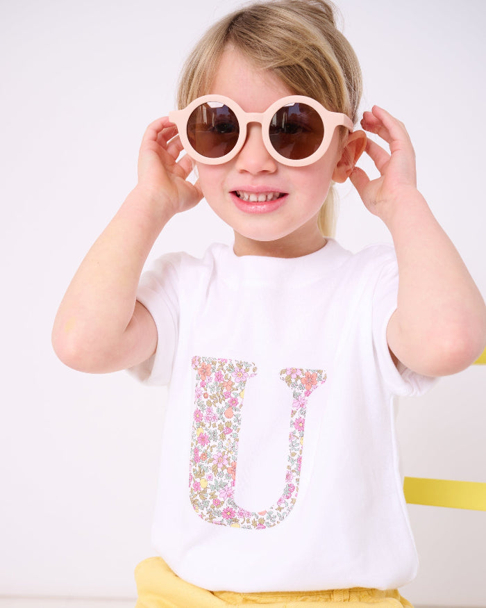 a child wearing a personalised white cotton T-Shirt with her initial letter on the front in Fruit Punch Liberty Print.