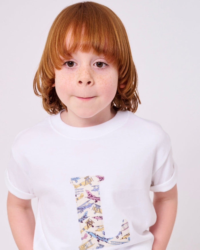 A boy wearing a personalised white cotton T-Shirt with his initial letter on the front in Toms Jet plane Liberty print