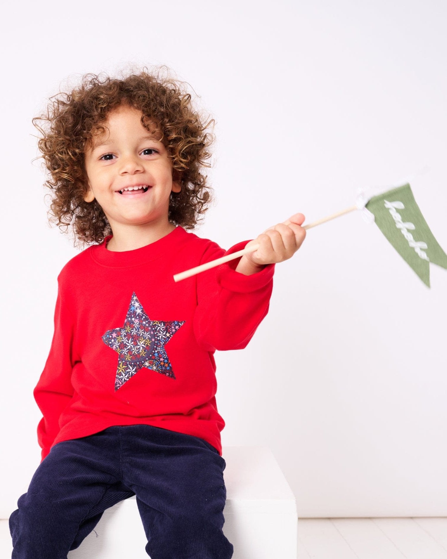A 3 year old boy wearing a red Christmas t-shirt with a liberty Adelajda's Wish star pritn fabric Christmas star appliquéd on the front.