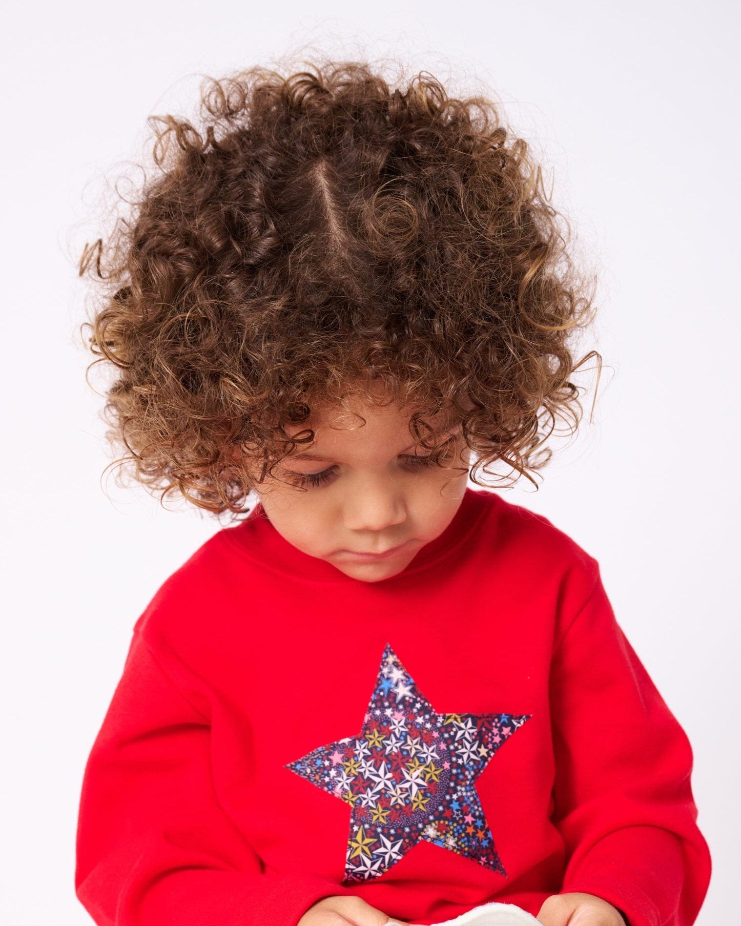 A 3 year old girl wearing a red Christmas t-shirt with a liberty floral Christmas star appliquéd on the front. She is holding a matching crown and wand.