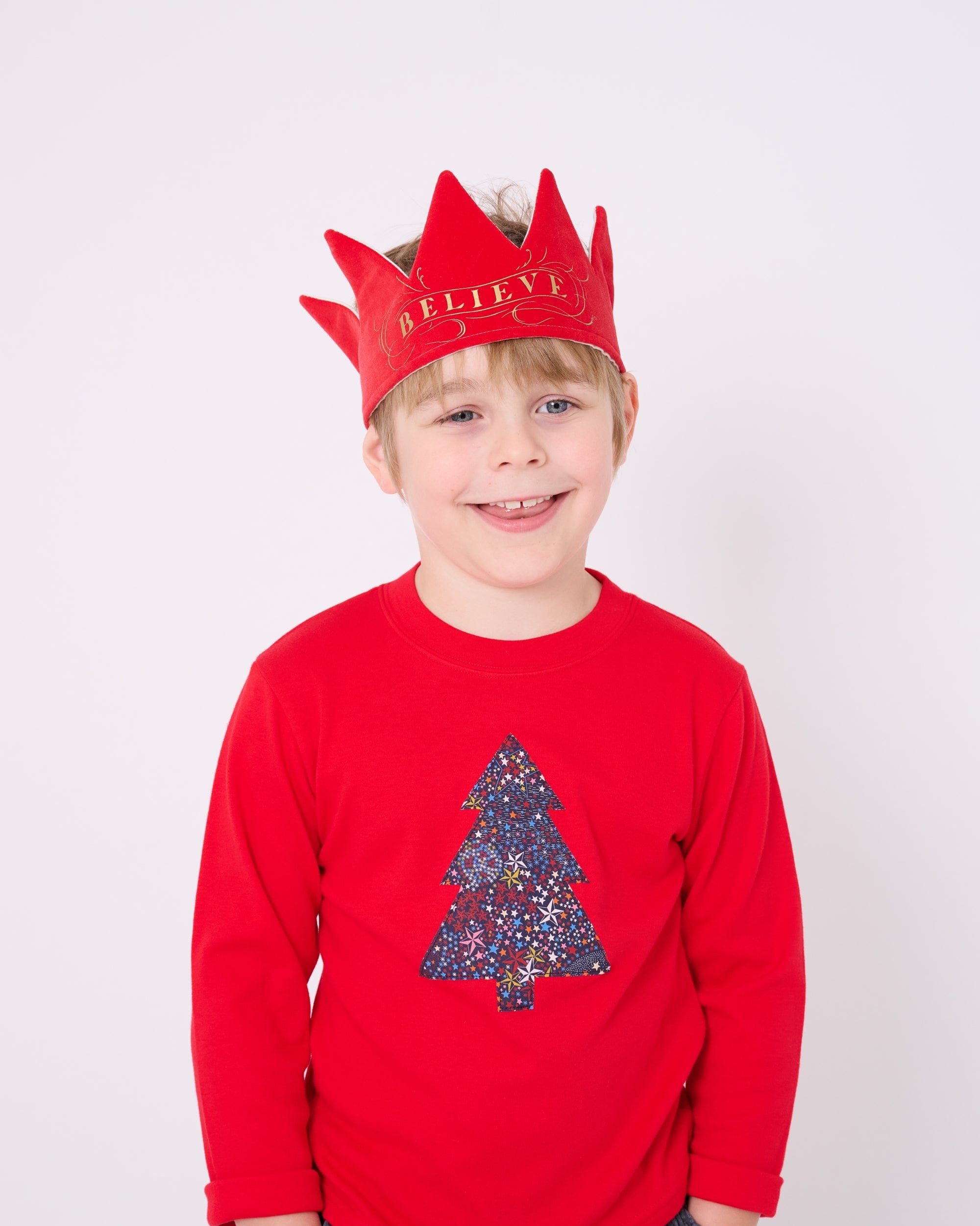 A 4 year old boy wearing a festive red cotton t-shirt with a christmas tree made from Liberty star Adelajda's Wish fabric appliquéd on the front.