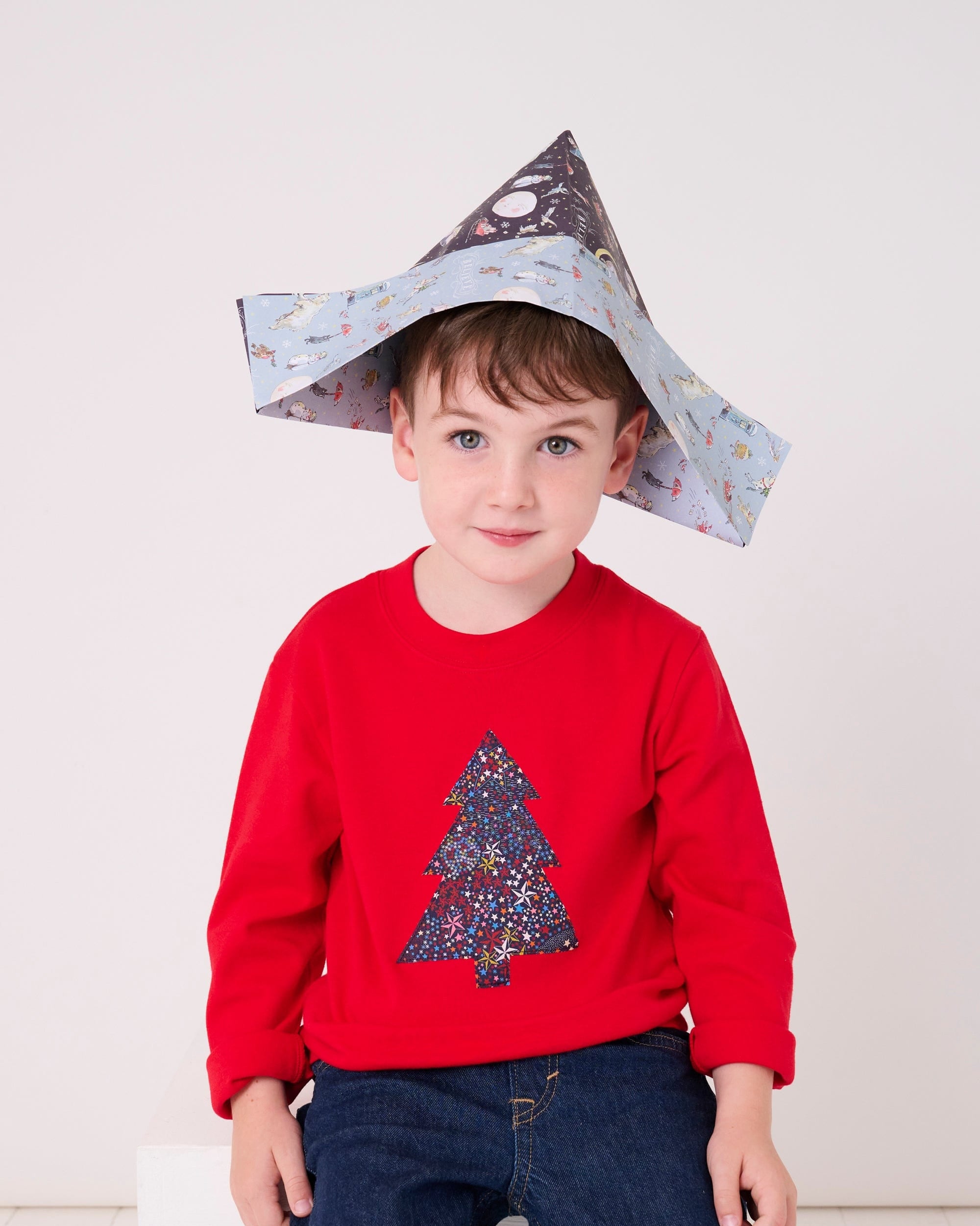 A 4 year old boy wearing a festive red cotton t-shirt with a christmas tree made from Liberty star Adelajda's Wish fabric appliquéd on the front.