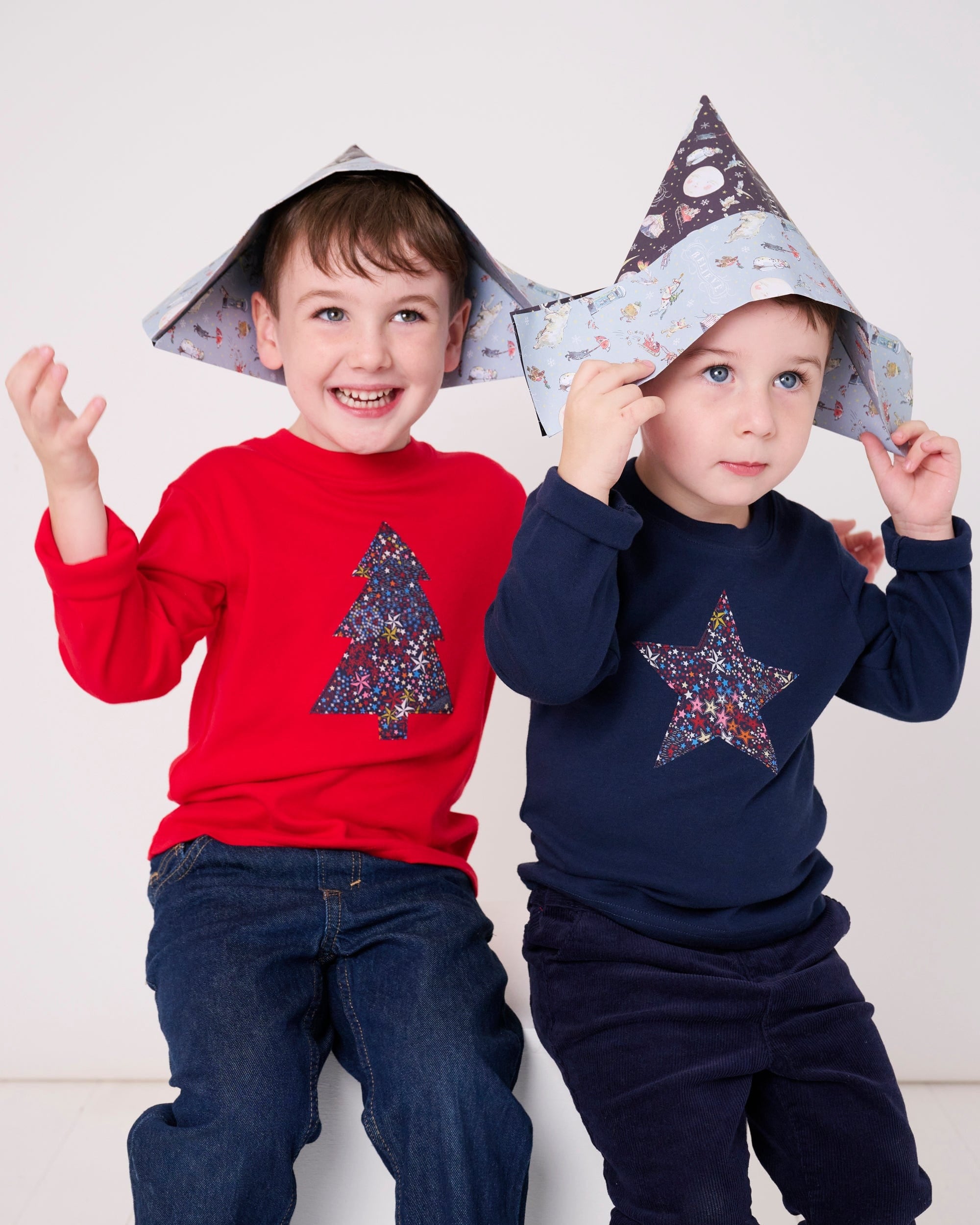 A 3 year old and 4 year old wearing a festive red and navy cotton t-shirts with a christmas tree and star made from Liberty star Adelajda's Wish fabric appliquéd on the front.