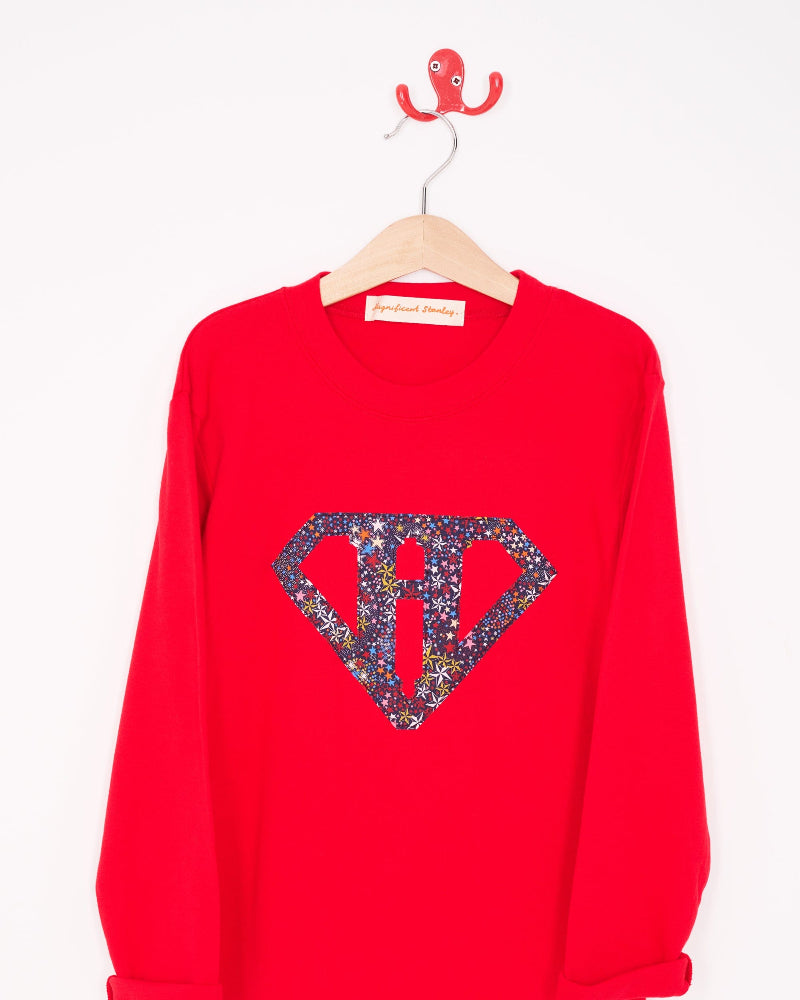 A red cotton personalised t-shirt with his initial in a superhero emblem Liberty star Adelajda's Wish fabric appliquéd on the front.