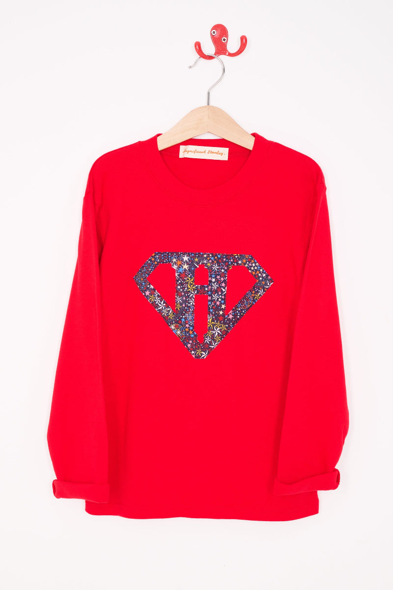 A red cotton personalised t-shirt with his initial in a superhero emblem Liberty star Adelajda's Wish fabric appliquéd on the front.