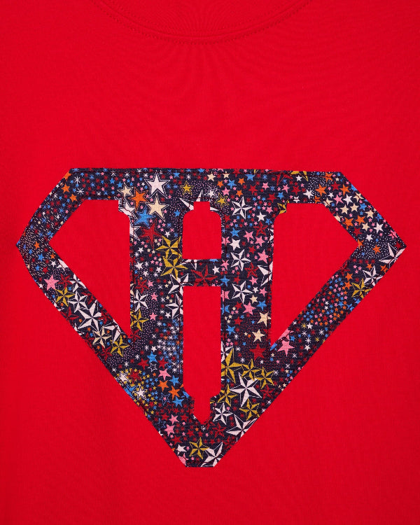 A close up of a red cotton personalised t-shirt with his initial in a superhero emblem Liberty star Adelajda's Wish fabric appliquéd on the front.