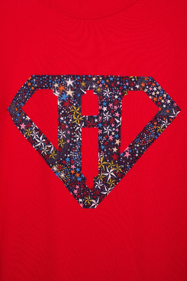 A close up of a red cotton personalised t-shirt with his initial in a superhero emblem Liberty star Adelajda's Wish fabric appliquéd on the front.