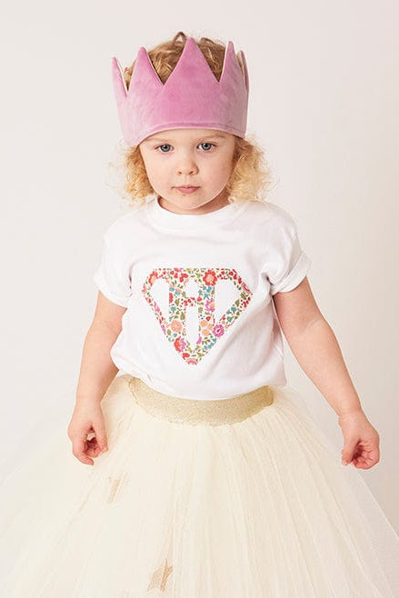 A 3 year old girl wearing a personalised white t-shirt with a superhero motif initial made from floral Liberty print fabric.