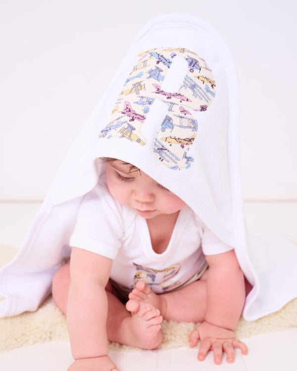 A little baby wearing a soft cotton hooded baby towel with his initial sewn on the hood in jet plane liberty print.