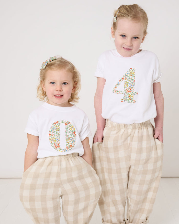 A 2 year old and a 4 year old wearing matching summery personalised white cotton t-shirts with an initial cut from Nazanin floral liberty fabric.