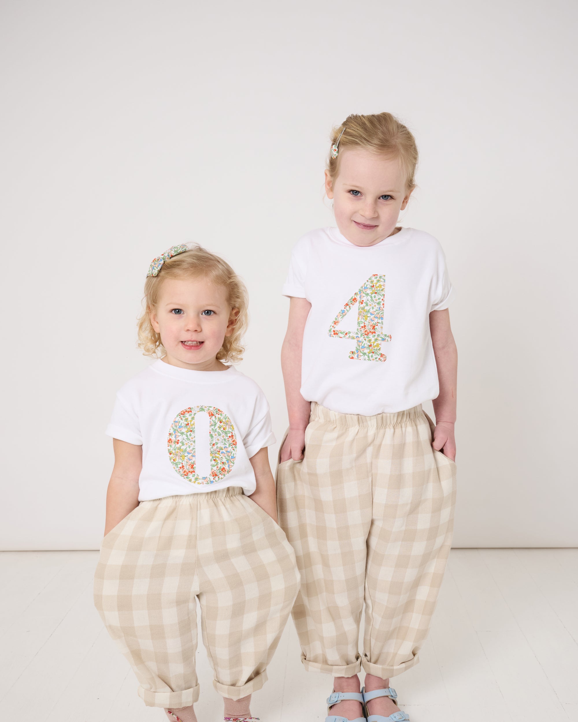 A 4 year old girl wearing a white cotton birthday t-shirt with the number 4 sewn on the front cut from liberty Nazanin fabric. She is in a matching outfit with her little sister.