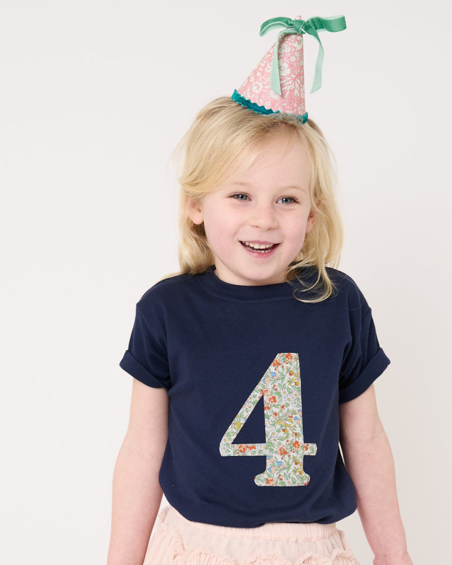 A girl celebrating her 4th birthday wearing a navy cotton t-shirt with the number 4 sewn on the front cut from liberty floral Nazanin print.