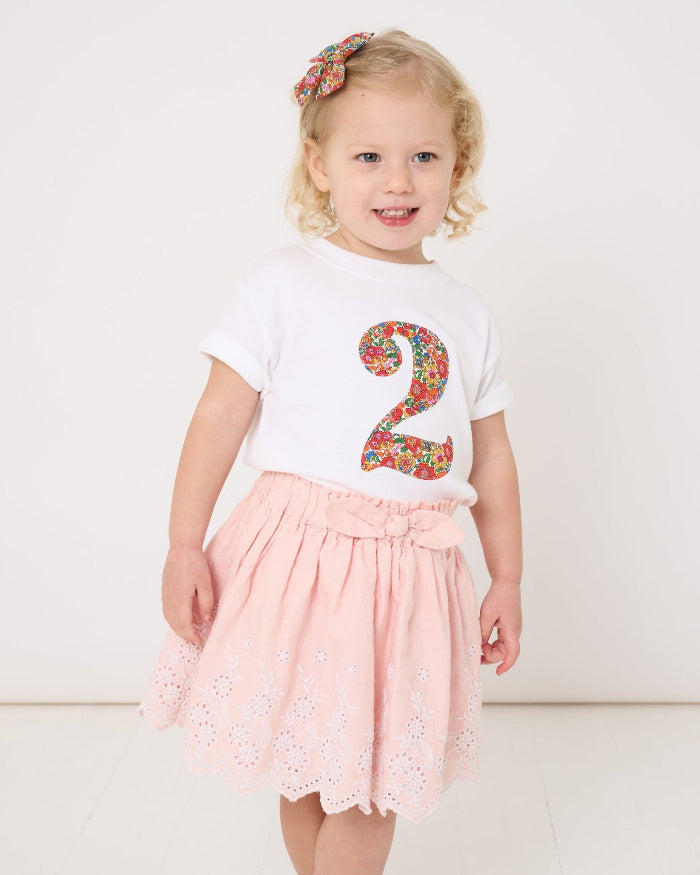 A 2 year old girl wearing a white cotton birthday t-shirt with the number 2 sewn on the front cut from liberty Nell Annie and May fabric.