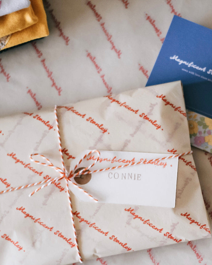 a gift wrapped item with branded tissue paper and striped twine with a hand stamped name tag.