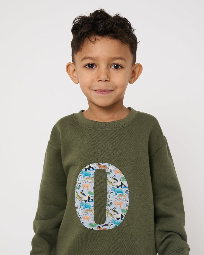 Child wearing a personalised khaki sweater with a large letter 'O' in Quey 2 liberty animal print.