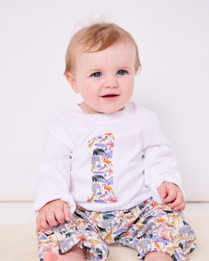 A 1 year old boy wearing a birthday white cotton t-shirt with the number 1 on in queue for the zoo Liberty fabric.