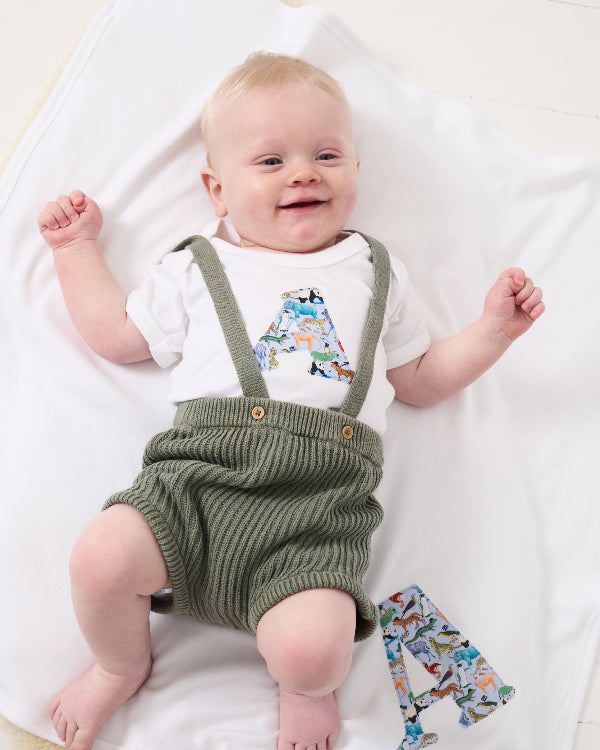 a smiling baby wearing a personalised baby bodysuit made from Liberty zoo animal print Quey 2 on a matching personalised blanket