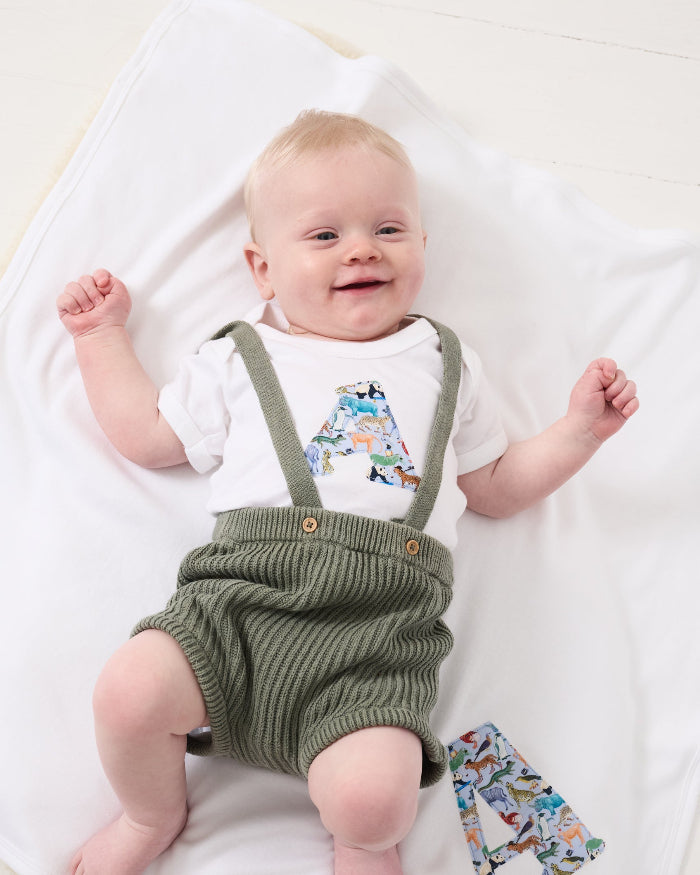 A newborn baby laying on Personalised Liberty Print Cotton Baby Blanket with their initial sewn on it.