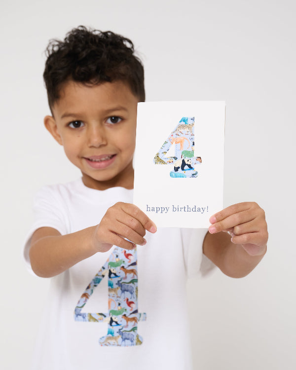 A 4 year old boy wearing a white cotton t-shirt with the number 4 sewn on the front cut from liberty Quey 2 zoo animal print. He is holding a matching number 4 birthday card
